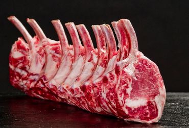 Raw rack of lamb with visible marbling on a dark surface.