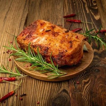 Roasted meat garnished with rosemary and chili peppers on a wooden plate.