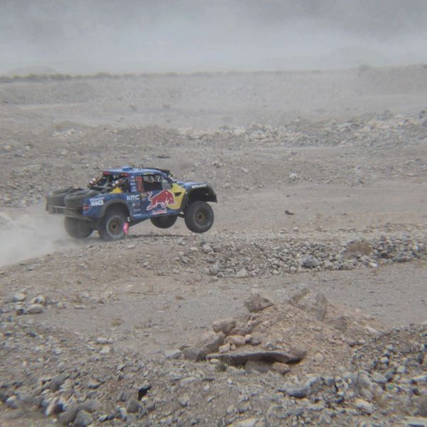Off-road racing truck airborne over rocky terrain.