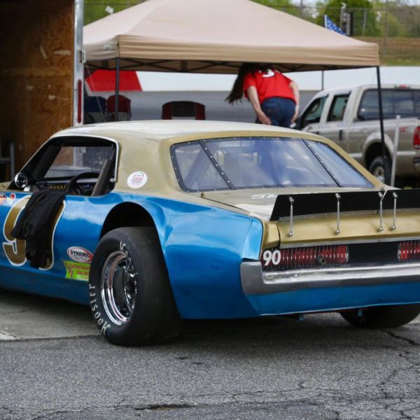 Blue and gold race car parked with a tent and person in background.
