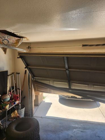 Partially broken garage door hanging unevenly with items stored inside the garage.