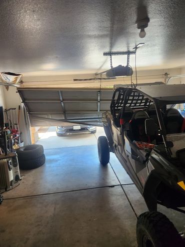 Damaged garage door bent inward with a side-by-side vehicle inside.