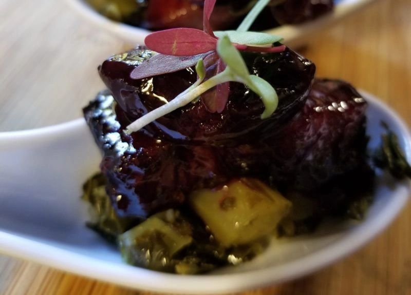 Close-up of a gourmet bite with glazed meat and microgreens.