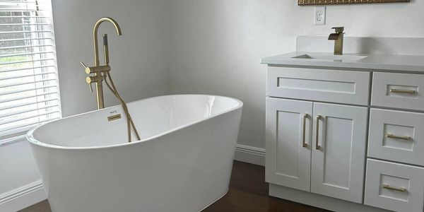Modern bathroom with white shaker cabinets with gold fixtures with a free standing tub