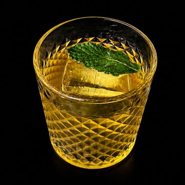 Glass of whiskey with a mint leaf on top, served with ice.