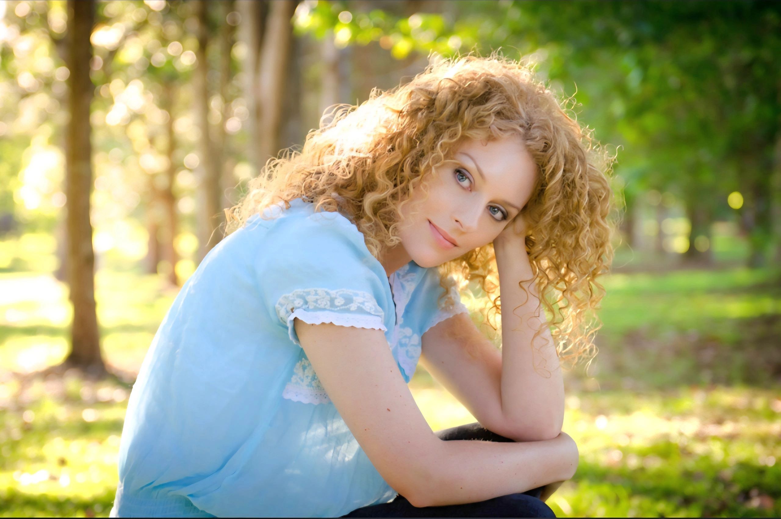 Pennyanne Lace, woman with blonde hair blue shirt and jeans sun light behind her outdoors tree