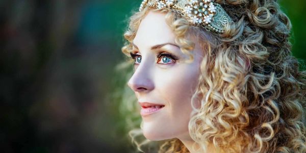 A serene profile of a blue‑eyed figure wearing an ornate golden headpiece with pearls and gems.