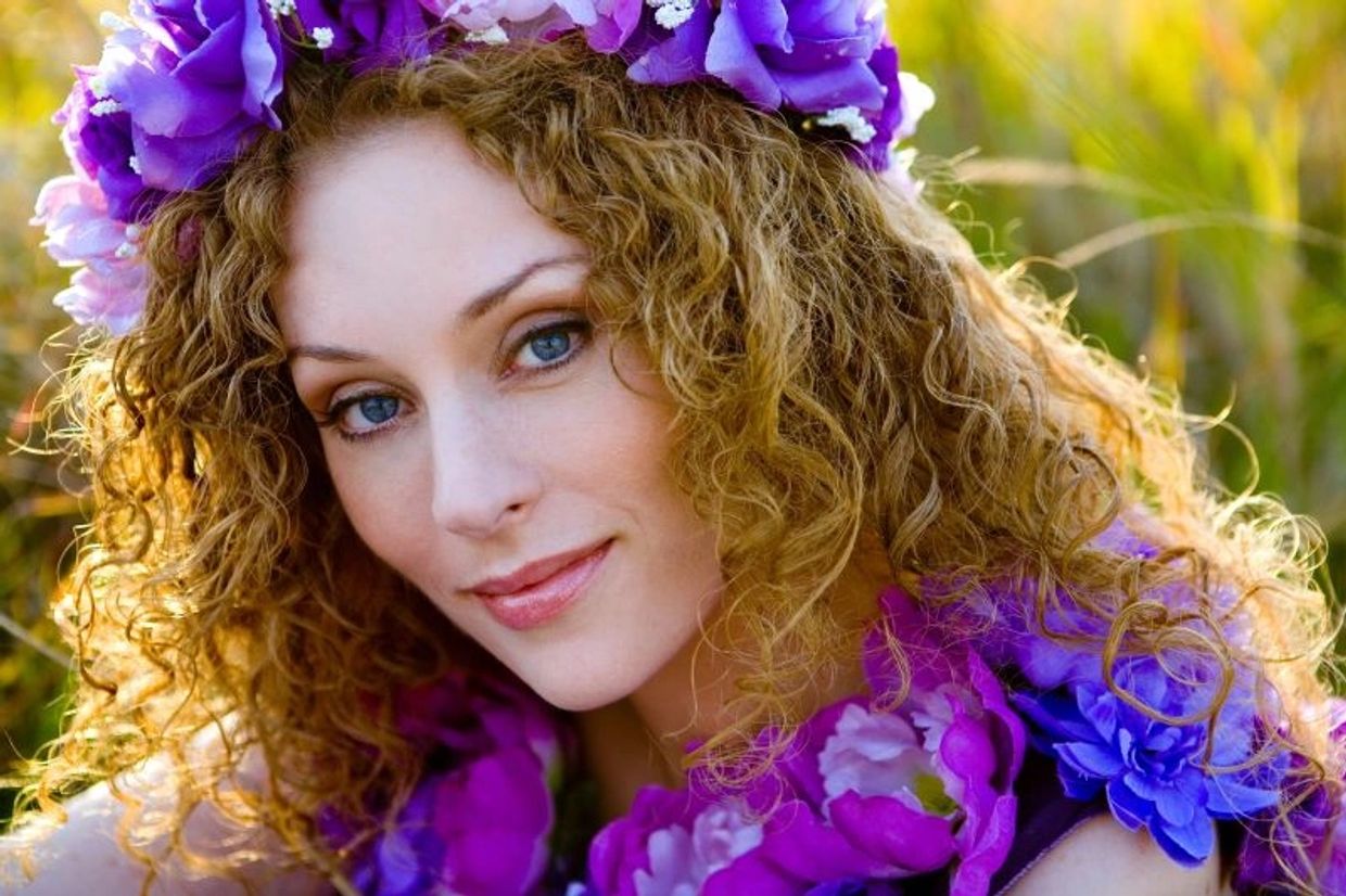 Pennyanne Lace wearing purple flower wreath on her curly blonde hair with matching flower collar.