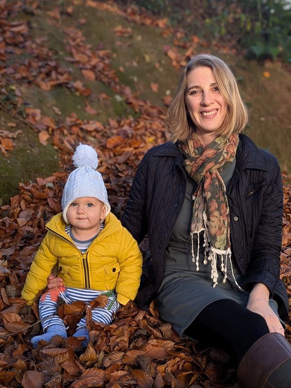 A woman and baby sitting on autumn leaves, smiling gently at the camera.
