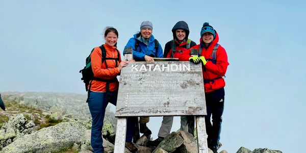 Four hikers posing by the Katahdin summit sign in foggy weather.