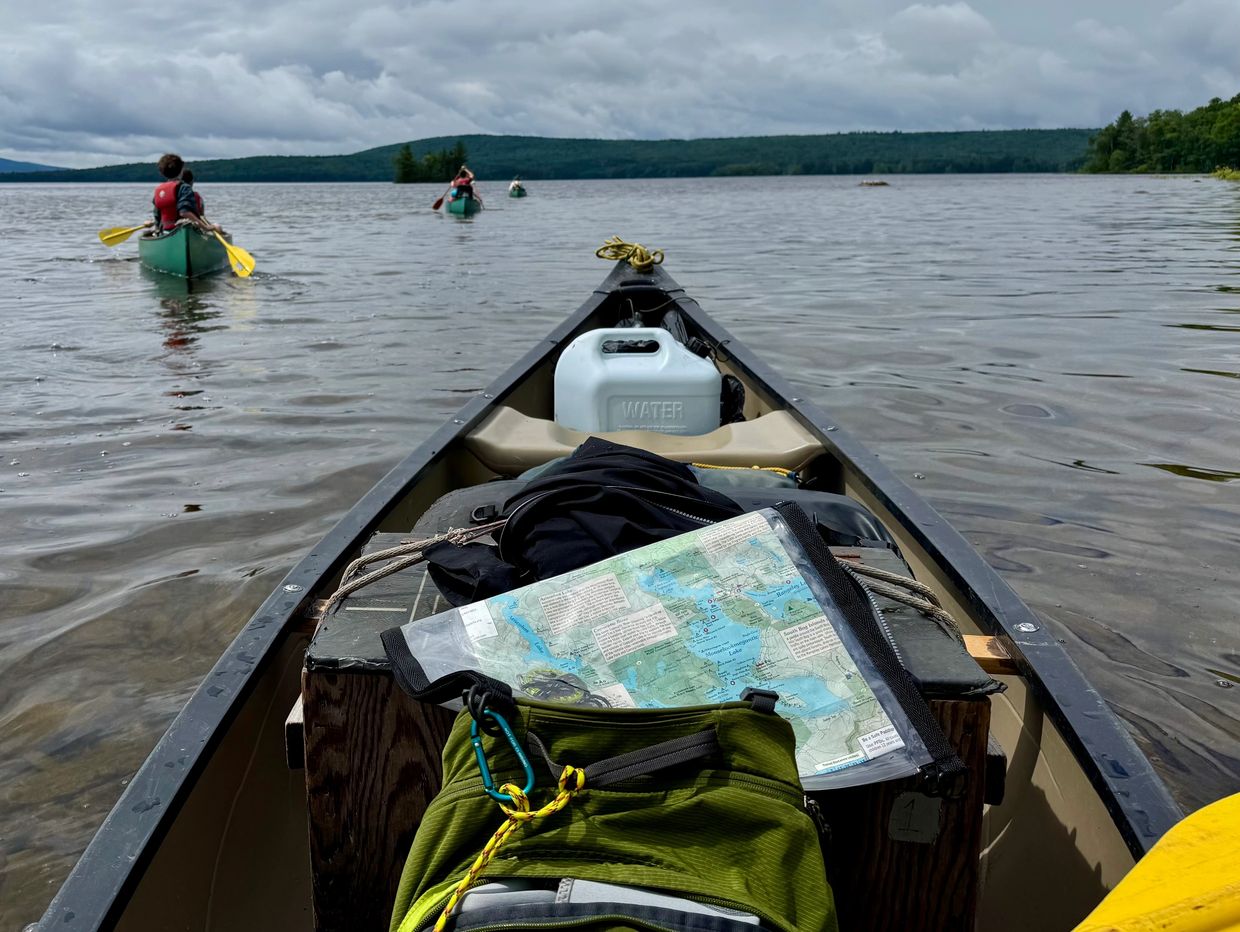 View from a canoe on a lake with other canoes ahead and outdoor gear inside.