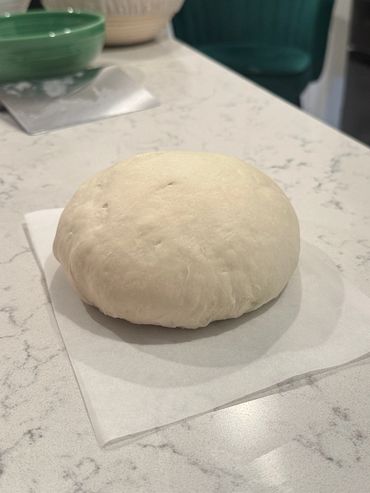 A ball of risen pizza dough on parchment paper.