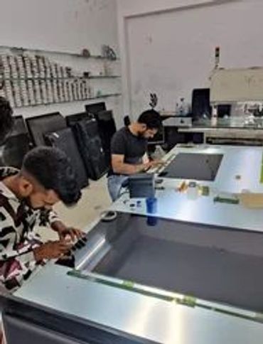 Two men repairing or assembling electronic devices on a table in a workshop.