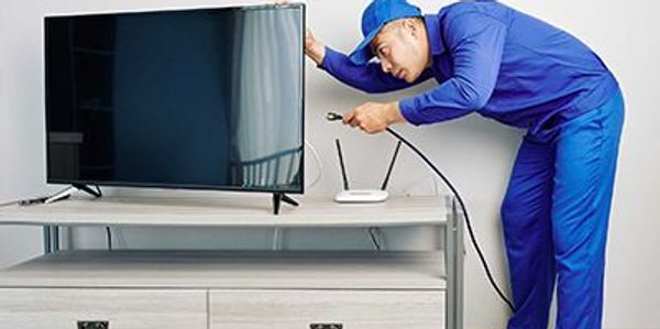Technician setting up internet connection behind a TV in a living room.