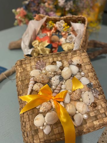 A woven basket lid decorated with seashells, pearls, and a yellow satin ribbon bow.