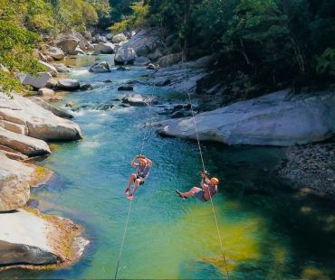 Dos personas cruzan un río colgando de cuerdas.