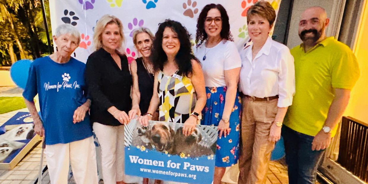 Group of people posing with a Women for Paws banner at an outdoor event.