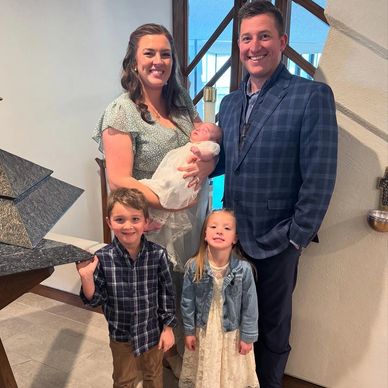 Family portrait with parents and three children, including a newborn in a white dress.