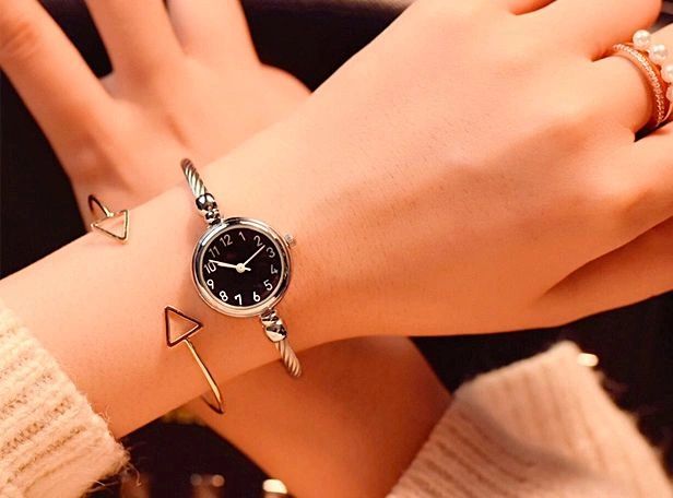 Elegant wristwatch with black dial and silver bracelet, paired with a stylish triangular bracelet.