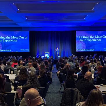Speaker presenting at a large conference with audience engaged.