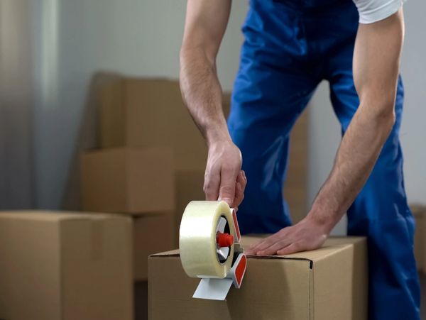 Person sealing a cardboard box with packing tape.