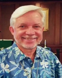 Smiling elderly man in a blue floral shirt.