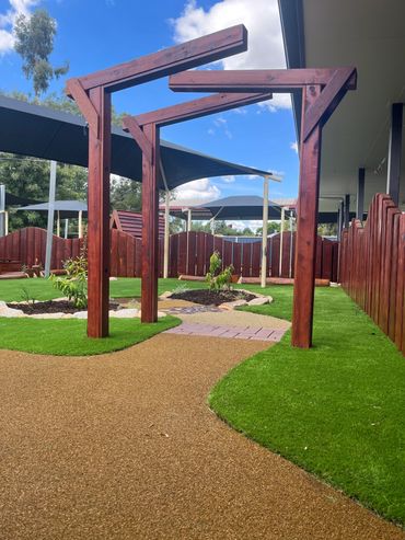 Wooden pergola structure over a garden path with green grass and blue sky.