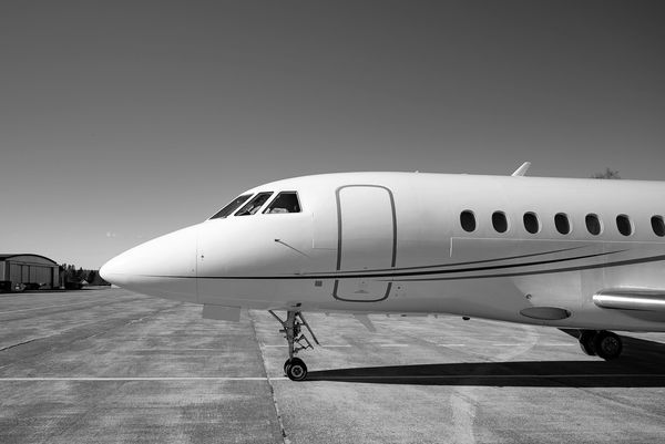 Black and white photo of a private jet on the tarmac under clear skies.