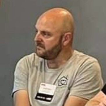 Bald man with beard wearing a gray shirt, looking sideways.