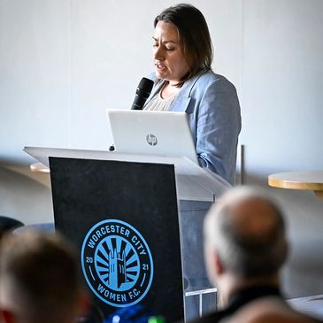 A woman speaks at a podium with Worcester City Women FC logo.