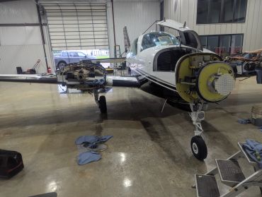 Small airplane undergoing maintenance with engine parts removed inside a hangar.