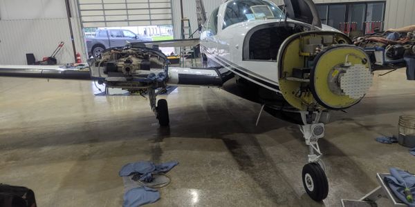 Small airplane undergoing maintenance with engine parts removed inside a hangar.