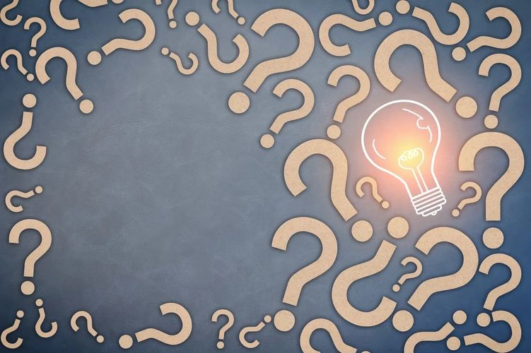 Glowing light bulb surrounded by scattered question marks on a gray background.