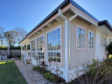 A cozy house with large windows and a brick path surrounded by a garden and lawn.