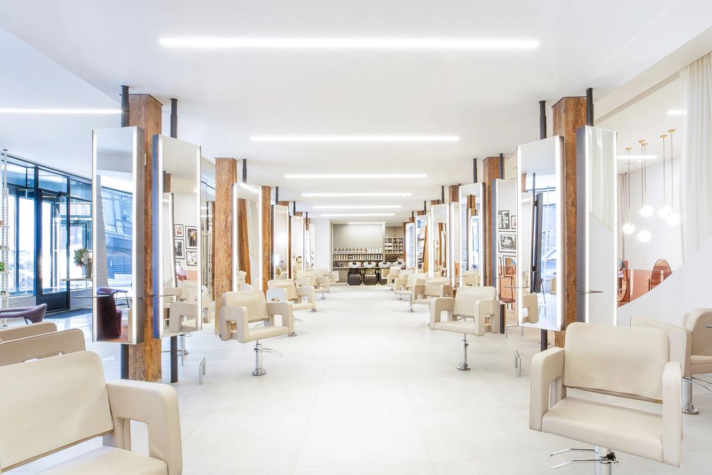 Bright, modern hair salon with beige chairs and wooden accents.