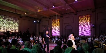 Two actors stand in the circular audience. One looks a way, while the other approaches her.