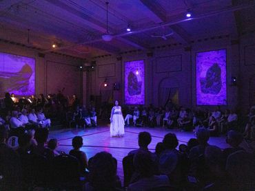 Actor stands center of a rope triangle, dark, purple lighting fills room.