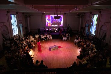 Above view of the room and ccircular audience seating. Actor walks around a center crate.