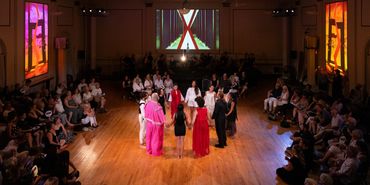 The ensemble holds hands in the center of the stage, forming a circle.