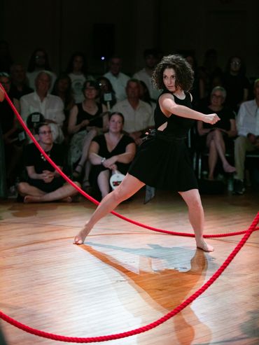 An actor dances inside a roped in space; the rope is red.