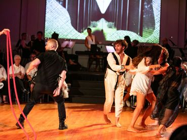 A few actors start to run away from a doorway made of rope, one turns and glances back.