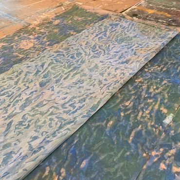 A painted curtain lays on the floor. It is painted with a mix of blues, greens, and browns.