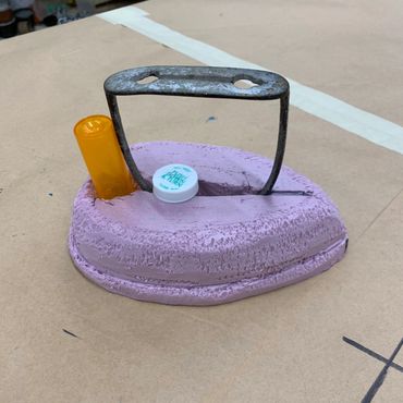 The structure of an iron created with pink foam, a pill bottle, and a horse stirrup.