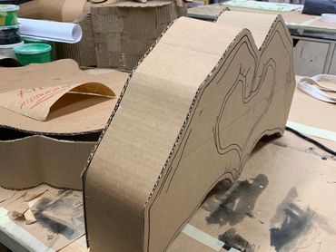 A cardboard structure stands on a table in the shape of two hands making a heart.