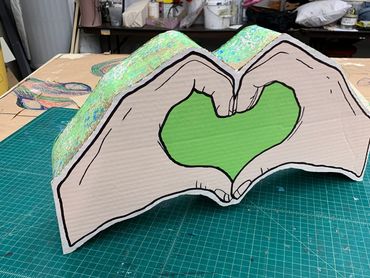 A cardboard structure in the shape of two hands is fully painted and finished.