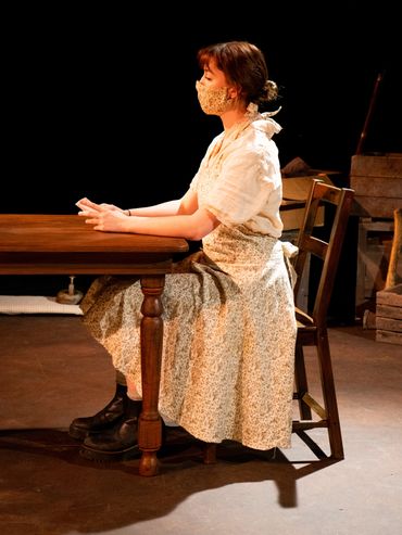 An actor sits at a table, she holds a small book in her hands.