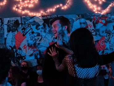 An actor turns another actor's face to the left. Behind, a collage filled with music and graffiti.
