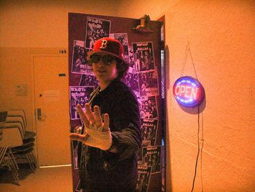 An actor stands in front of the entrance to the room with his hand up, stopping the viewer.