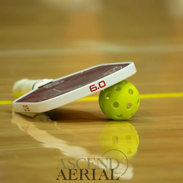 Pickleball paddle resting on a yellow pickleball on a wooden court.