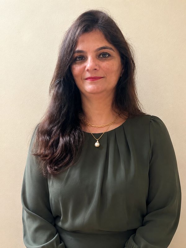 Woman with long dark hair wearing green top and gold necklace.